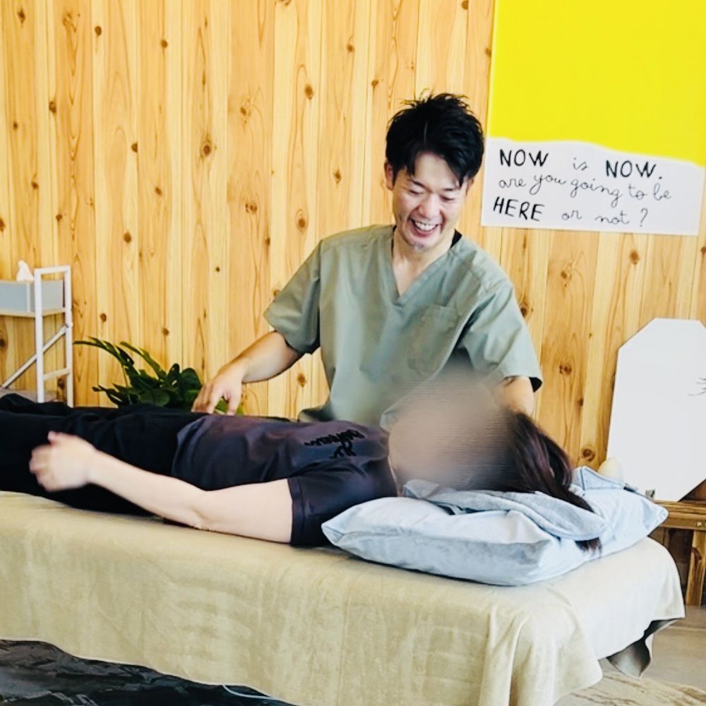 理学療法士の院長が、笑顔で、横になった利用者の体に手を添えている様子（利用者の顔はぼかしています）